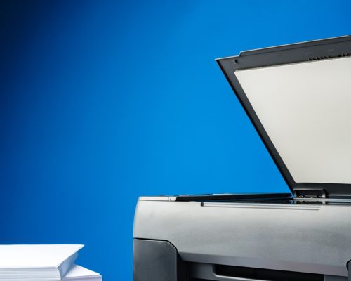 Laser printer on desk against blue background close up